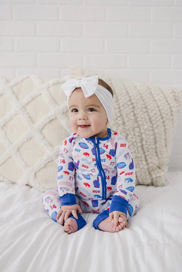 Baby in bamboo Buffalo football royal blue and red sleeper with number 17 and 86 print. Sitting on creme background.