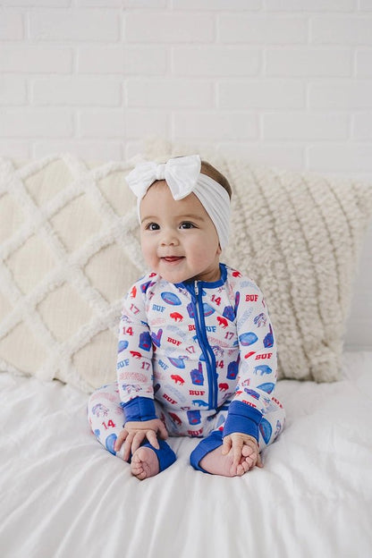 Baby in bamboo Buffalo football royal blue and red sleeper with number 17 and 86 print. Sitting on creme background.