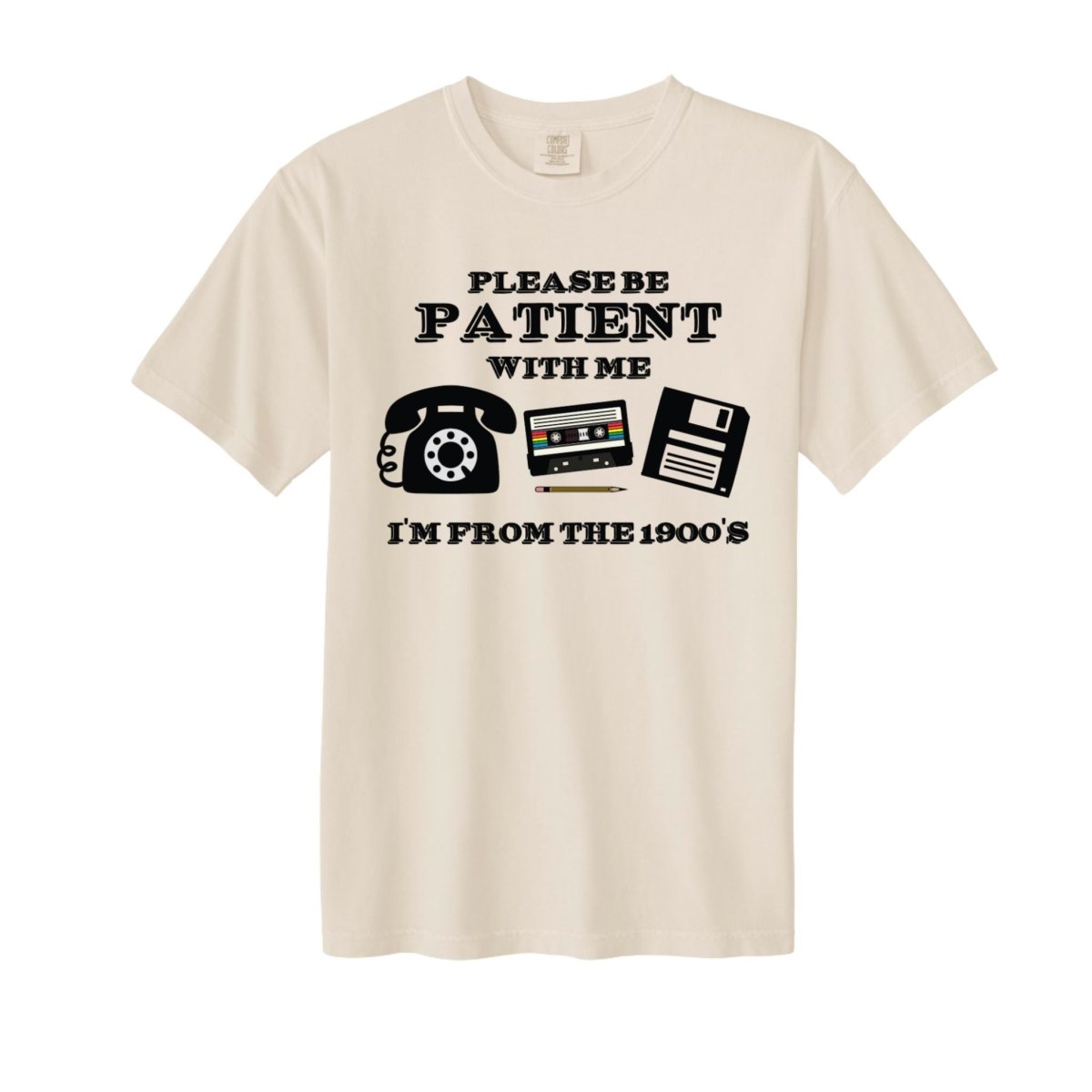 Beige tshirt with "Please be patient with me I'm from the 1900's" and old telephone, cassette tape, and floppy disc on front sitting on a white background. 