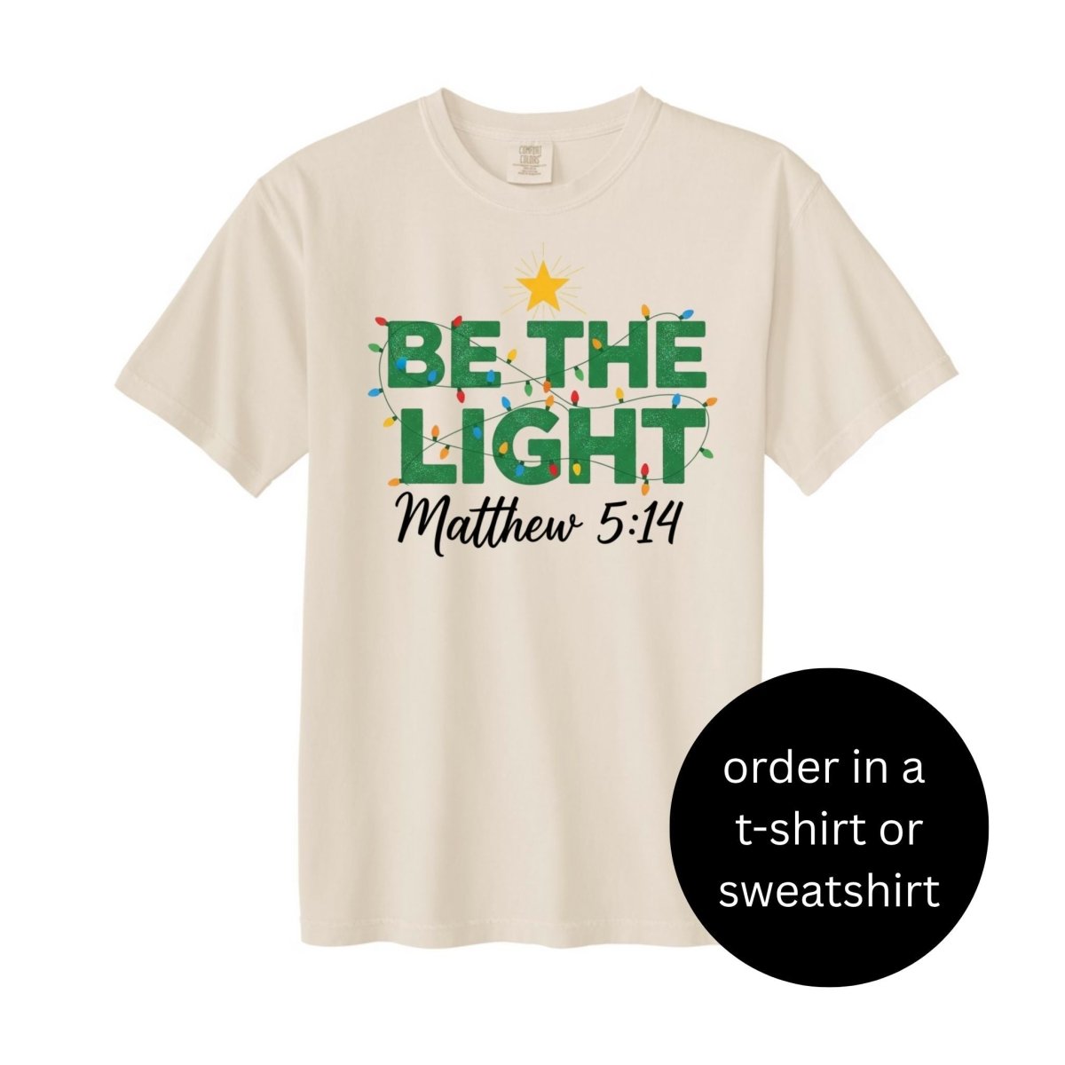 Creme green Be the Light Matthew 5:14 Christmas lights tshirt on white background. Little Gift Nook