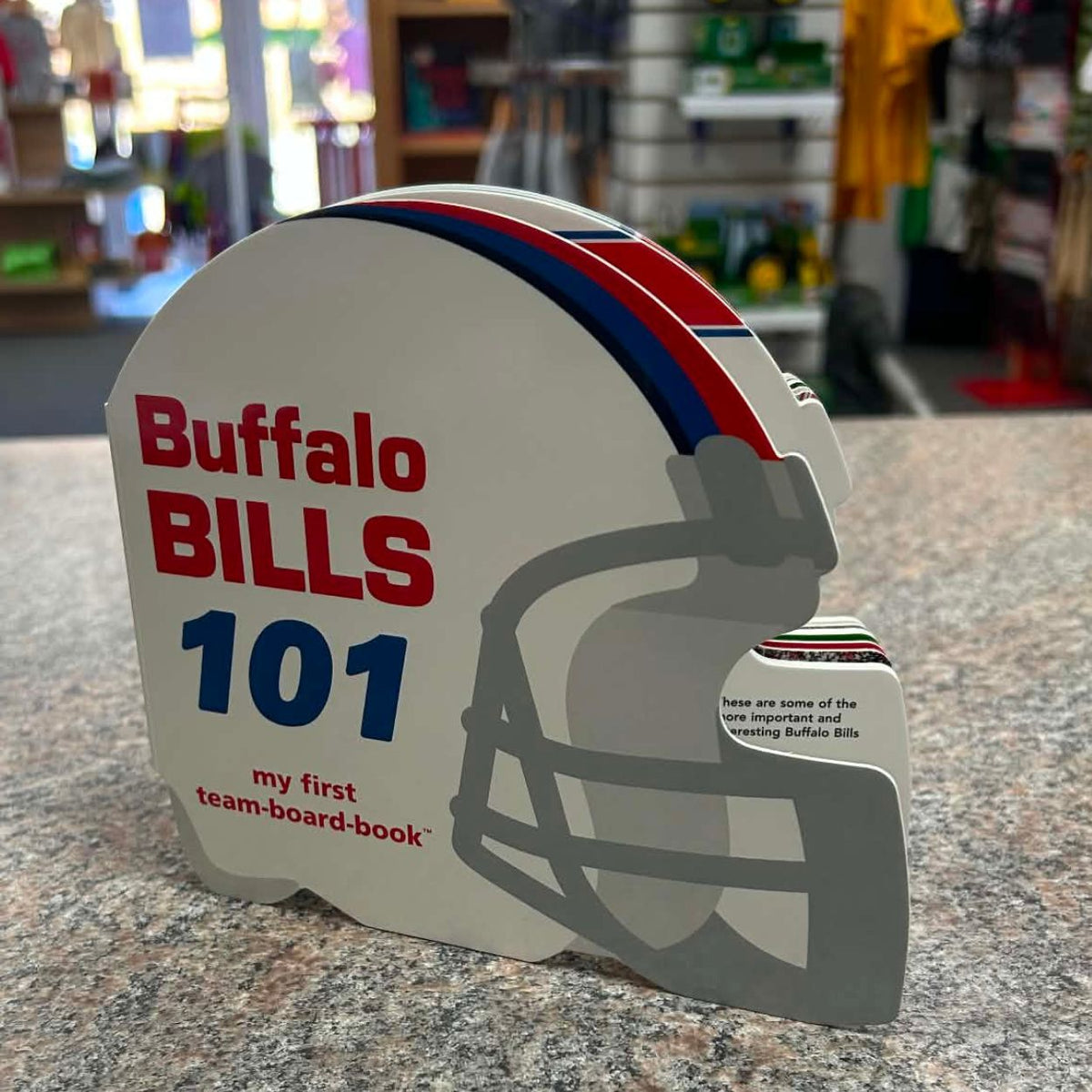 A Buffalo Bills themed children's team board book shaped like a football helmet, standing on a granite countertop with a blurred store background.
