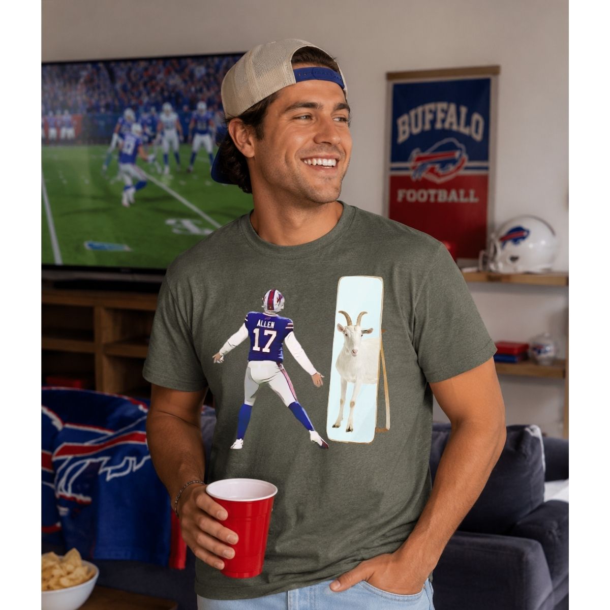 Man wearing gray Buffalo football Josh GOAT t-shirt standing in front of TV with football game on.