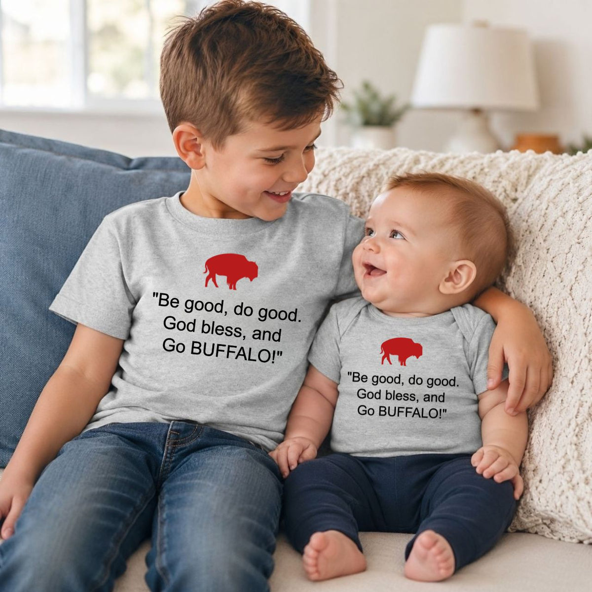 Little boy with baby brother on a couch wearing gray red buffalo tshirts with quote "Be good, do good, God bless, and go Buffalo!" on fronts.
