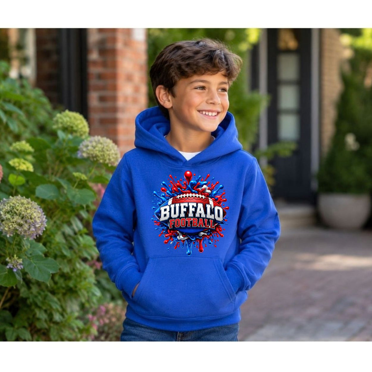 A young boy wearing a bright blue hoodie with a red, white, and blue 'Buffalo Football' graphic on the chest, standing outdoors in front of a house with green plants.