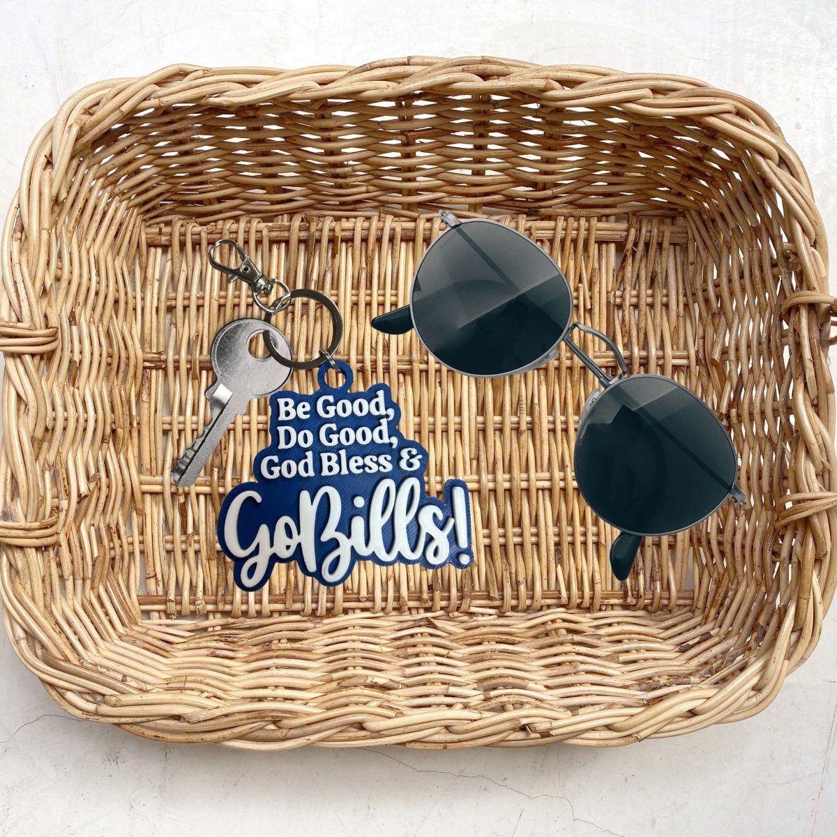 Wicker tray with buffalo football keychain mvp quote "Be Good, Do Good, God Bless and Go Bills!" and sunglasses on a light gray background. 
