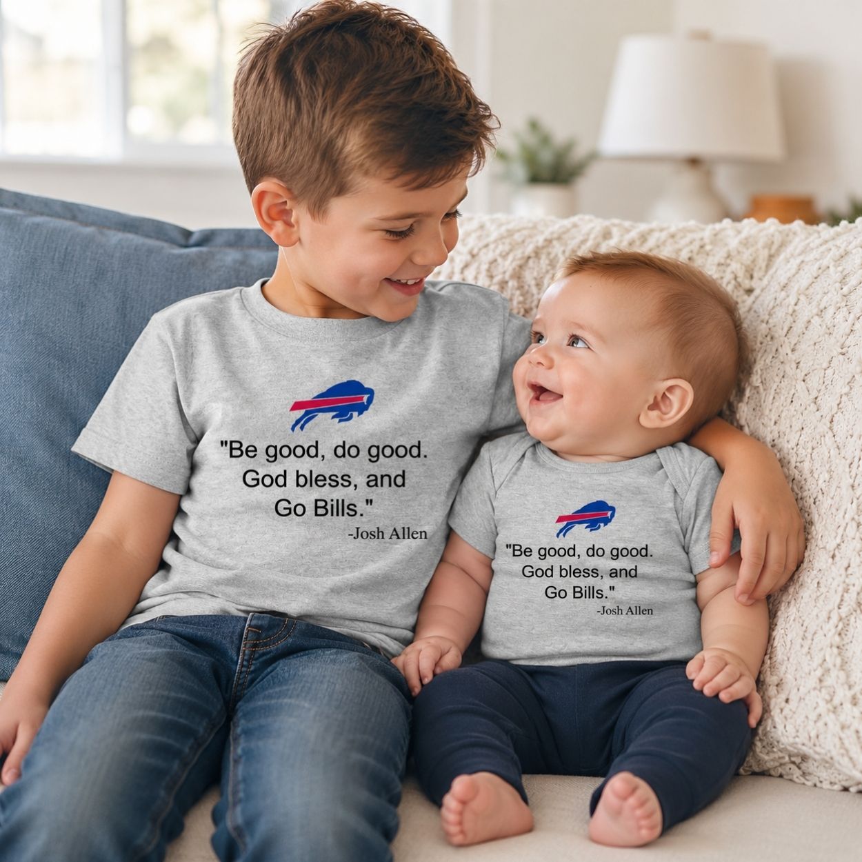 A young boy and a baby sitting together on a couch, both wearing matching light gray t-shirts with a Buffalo football MVP Josh Quote printed on the front.