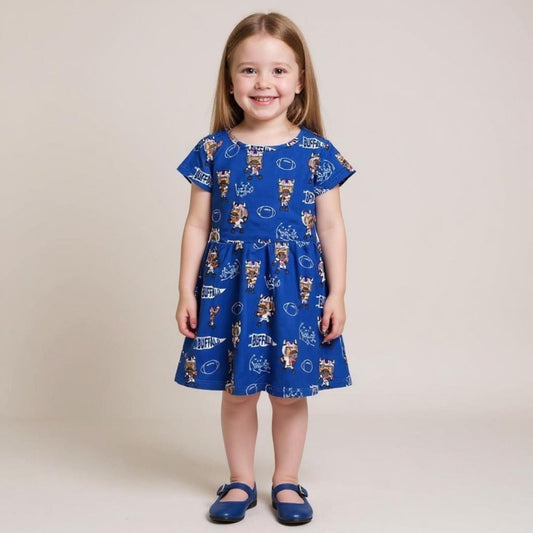 Little girl wearing royal blue cartoon buffalo football print dress with blue shoes on tan background. Little Gift Nook
