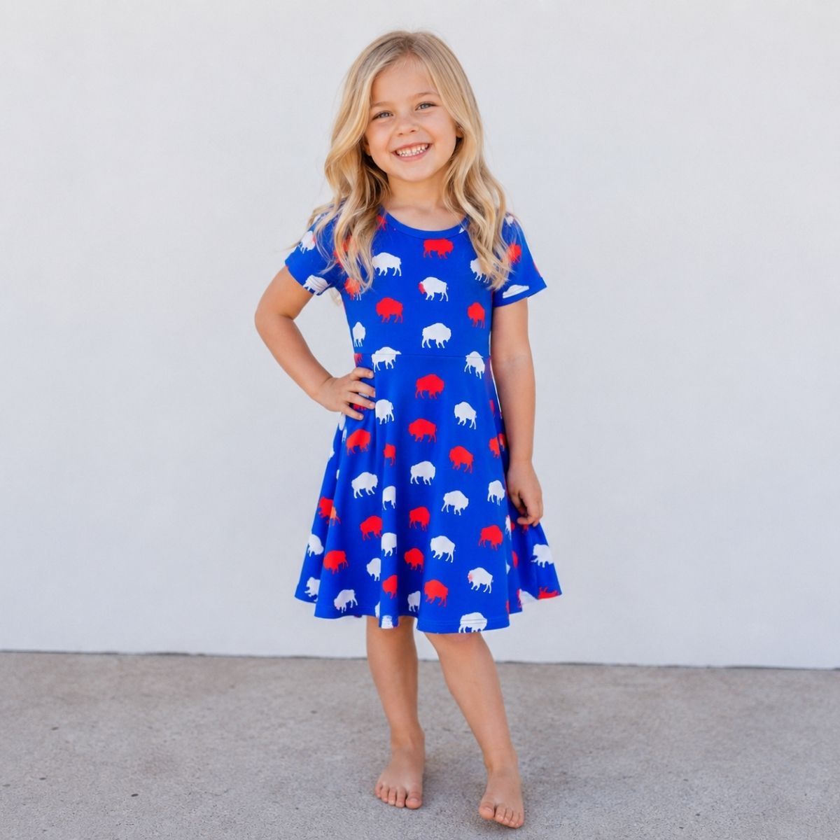 Little girl wearing royal blue twirl dress with red and white buffalo silhouette print standing on gray background - Little Gift Nook