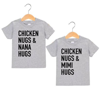 Two gray children's tshirts with black text "Chicken Nugs & Mama Hugs" and "Chicken Nugs & Mimi Hugs" on fronts hanging on hangers and on white background.