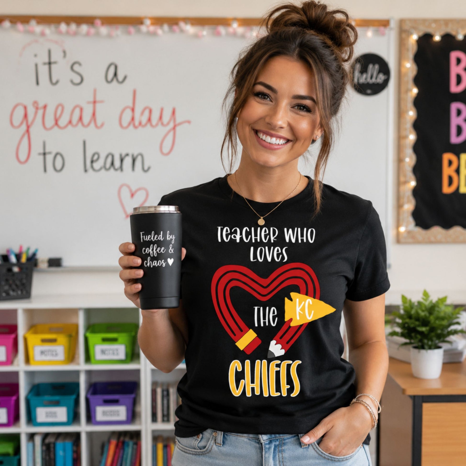 Woman in classroom wearing black "teacher who loves the KC Chiefs"tshirt holding a tumbler.
