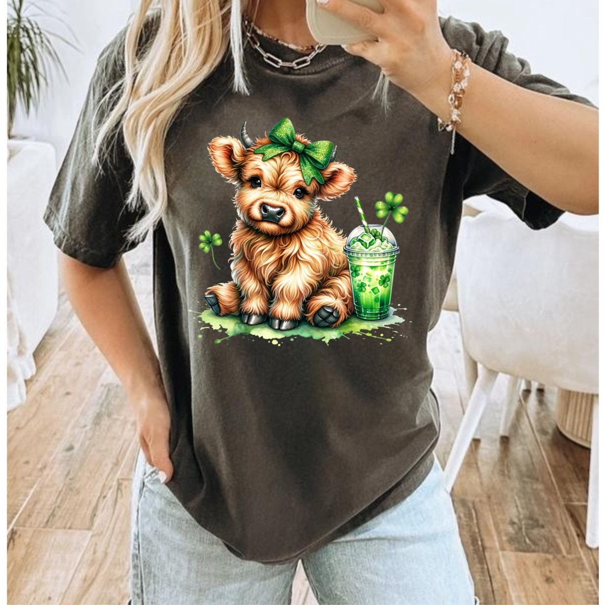 Woman wearing gray tshirt with image of brown cow in green hair bow with shamrock drink and clovers on front.