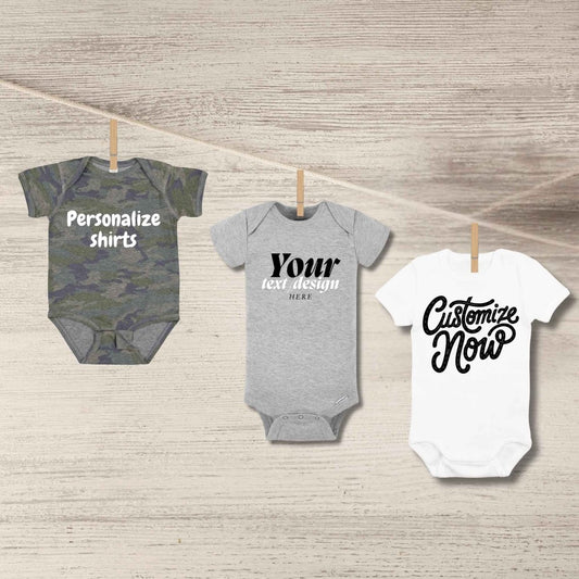 Custom baby onesies in camo, light gray, or white. Personalize baby onesies hanging from clothes pins on a wood background.  Little Gift Nook