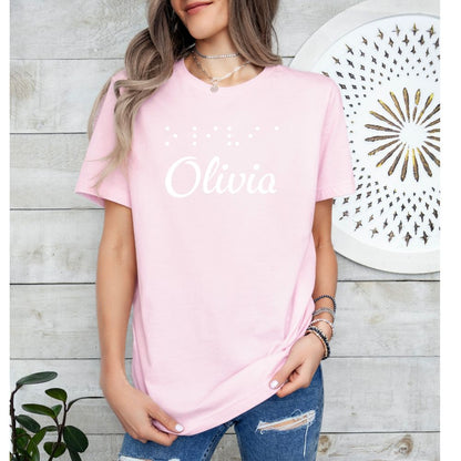 Woman wearing custom braille tshirt with name "Olivia" on front and braille raised puffy dots that spell name.