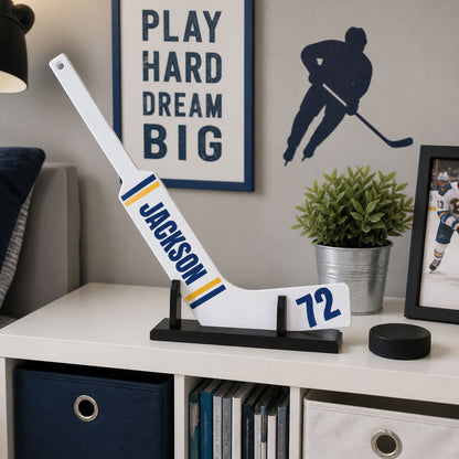 Mini hockey stick personalized with name JACKSON on front and 72 on a stand displayed near a wall of hockey memorabilia. 