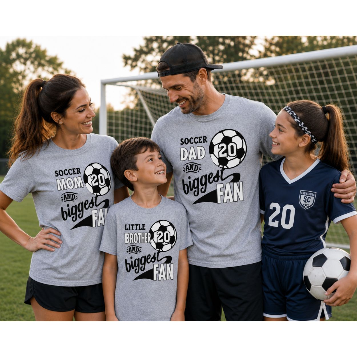 Sample custom t-shirts showing A family of four posing together on a soccer field wearing matching gray t-shirts with black and white soccer graphics and text. The shirts read 'SOCCER MOM AND biggest FAN', 'SOCCER DAD AND biggest FAN', and 'LITTLE BROTHER AND biggest FAN'.