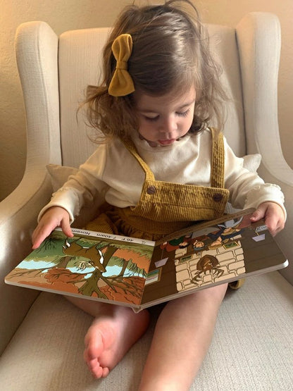 Little girl reading Deer Camp board book sitting in tan chair. 