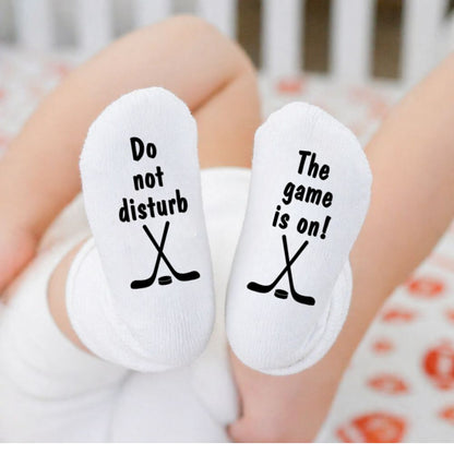 White baby socks with text and hockey stick graphics worn by a baby.