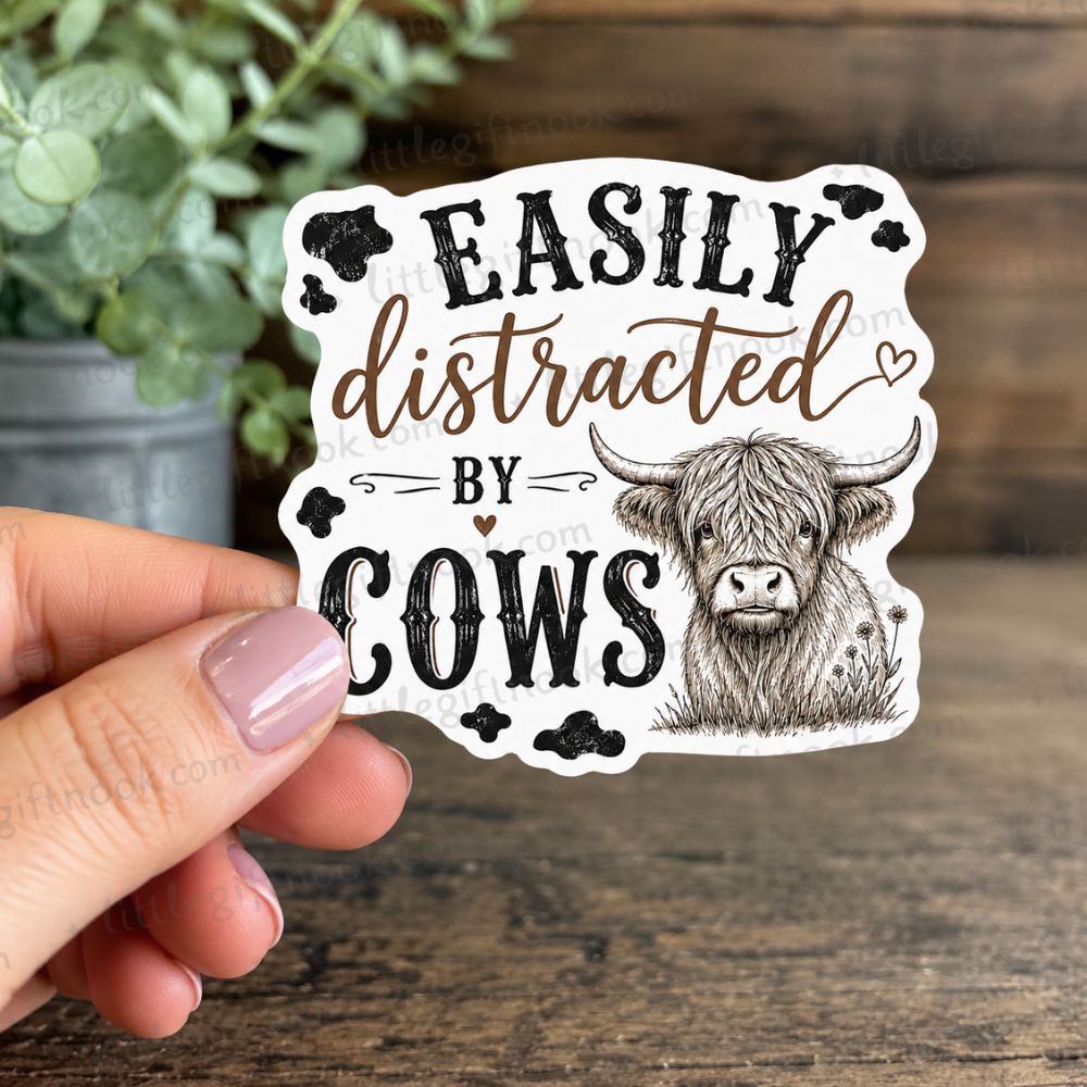 Sticker with a highland cow illustration and text "Easily distracted by cows" in black and brown text on a wood background.