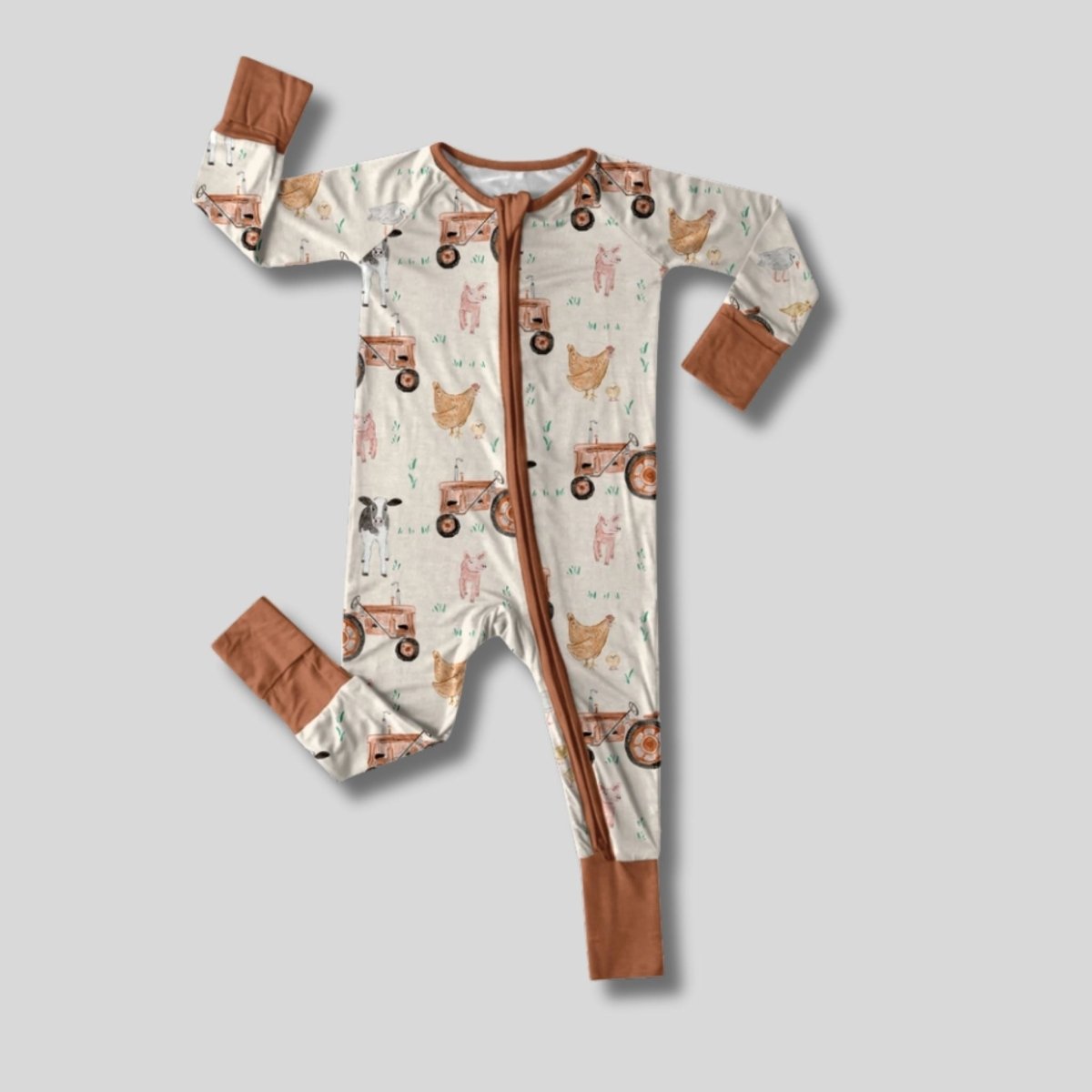 brown farm theme chickens, pigs, tractors print bamboo baby sleeper with fold over feet and hands on gray background. 