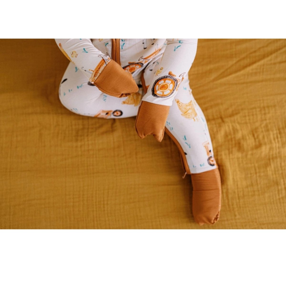 brown farm theme bamboo baby sleeper fold over feet and hands on mustard blanket background. 
