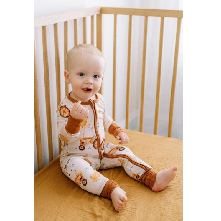 Baby sitting wearing brown farm theme bamboo sleeper in crib. 