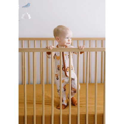 Baby standing in crib wearing brown farm theme bamboo sleeper.