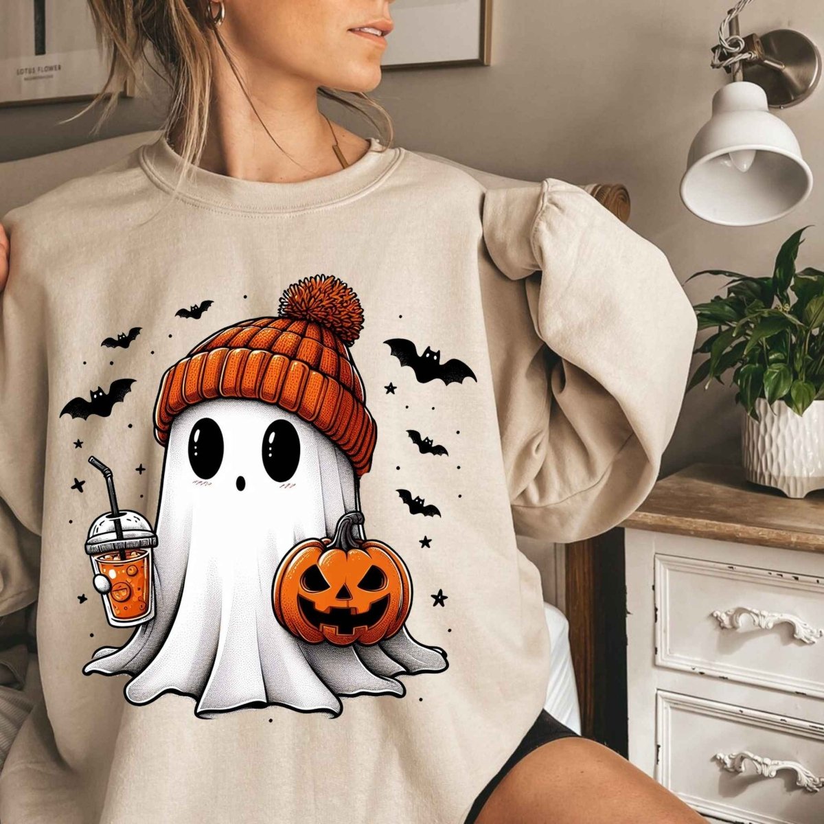 woman wearing beige orange beanie wearing ghost holding latte sweatshirt with furniture background. 