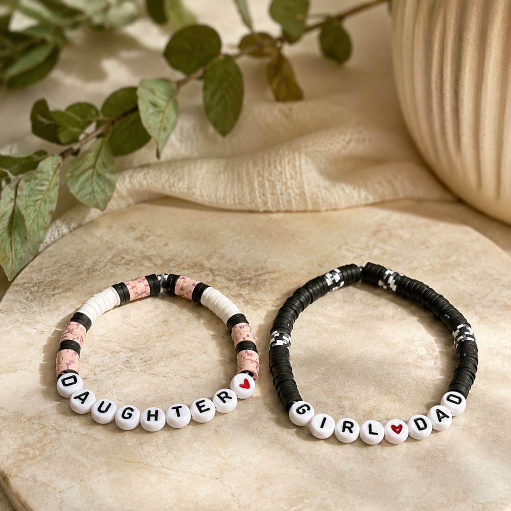 Two beaded bracelets with lettered beads "GIRL DAD" and "DAUGHTER" on a textured surface with greenery in the background.