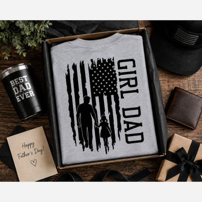 Gray t-shirt with 'Girl Dad' American flag design on back, folded in a box with Best dad ever tumbler and card on a wood surface.