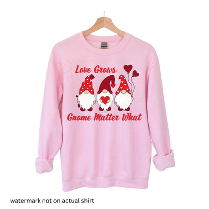 pink crewneck sweatshirt with 3 red gnomes and hearts "Love grows gnome matter what" on front hung on white background. Little Gift Nook