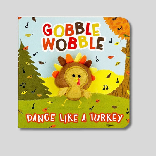Gobble Gobble Dance like a Turkey mini kids puppet board book with fall scene and little turkey puppet that pops through. Book sitting on gray background. 