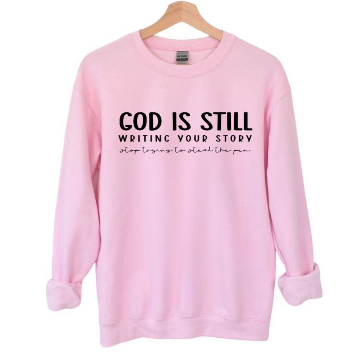 God Is Still Writing Your Story women's Pink Crewneck Sweatshirt. Light pink with black lettering on front. 