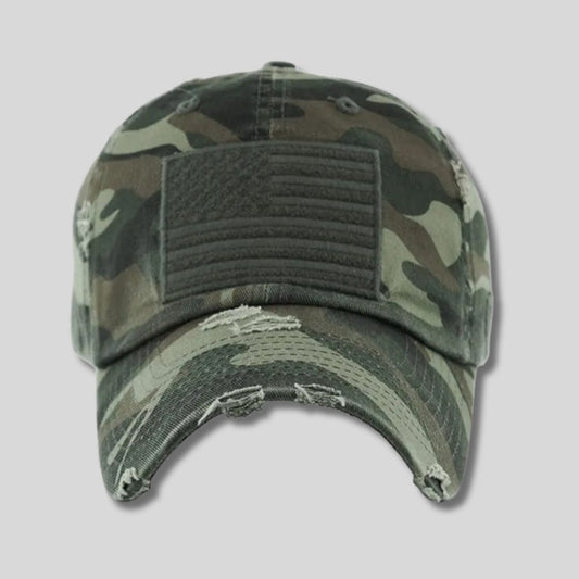 Green camo American Flag embroidered patch hat with distressed look sitting on a light gray background. Little Gift Nook