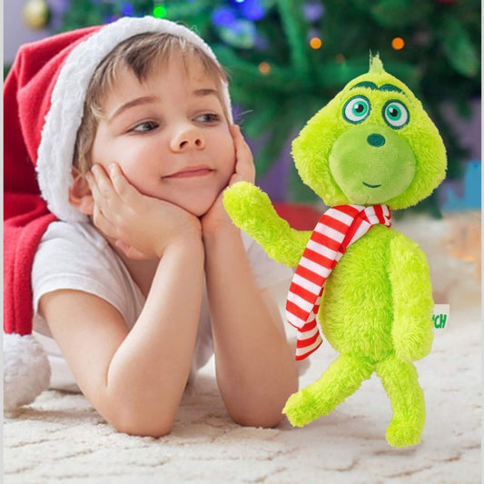 Child wearing a Santa hat with a green Grinch plush toy in front of a Christmas tree. Little Gift Nook
