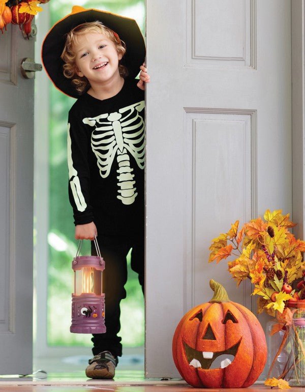 child in skeleton costume holding purple flickering flame pop up lantern in doorway with pumpkins. 