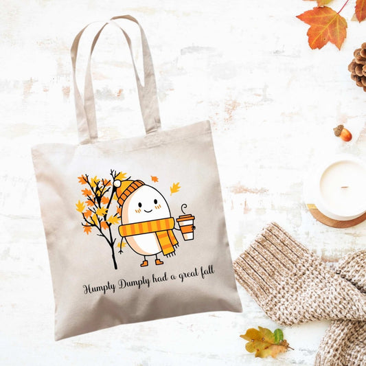 creme canvas tote bag with orange yellow fall leaves tree, humpty dumpty egg in hat and scarf holding a latte. Says "Humpty Dumpty had a great fall" in black text under image. Little Gift Nook