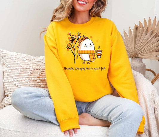 woman wearing golden yellow crewneck sweatshirt with 'humpty dumpty had a great fall' holding latte on front.