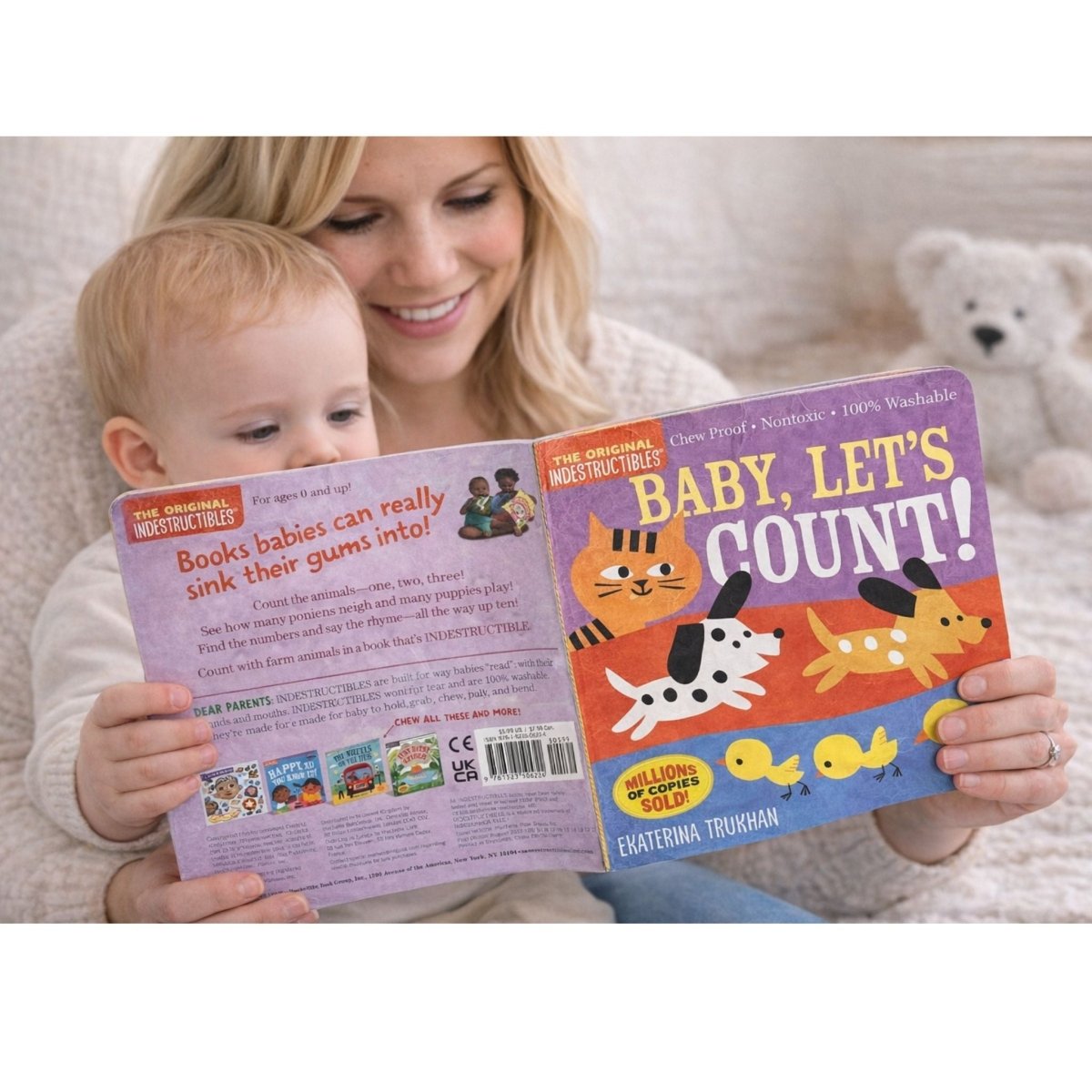 Woman and child reading a Indestructible book titled 'Baby, Let's Count!' with colorful illustrations on a soft surface.