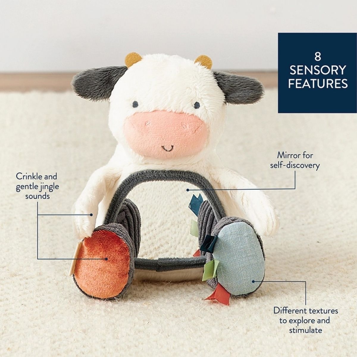 Itzy Ritzy plush  mirror cow texture baby toy.  Soft plush cow with crinkle & jingle sounds, tags and mirror on belly sitting on creme background with features.