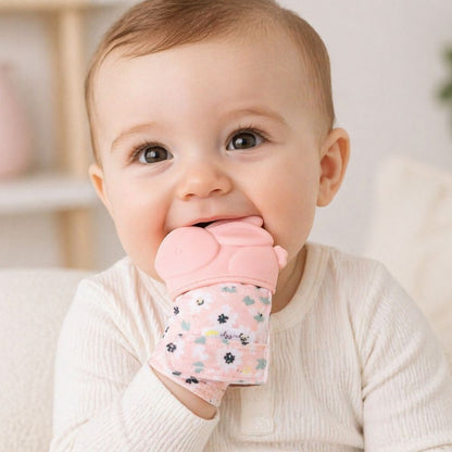 Baby wearing pink bunny teething mitt chewing on it on a white background.