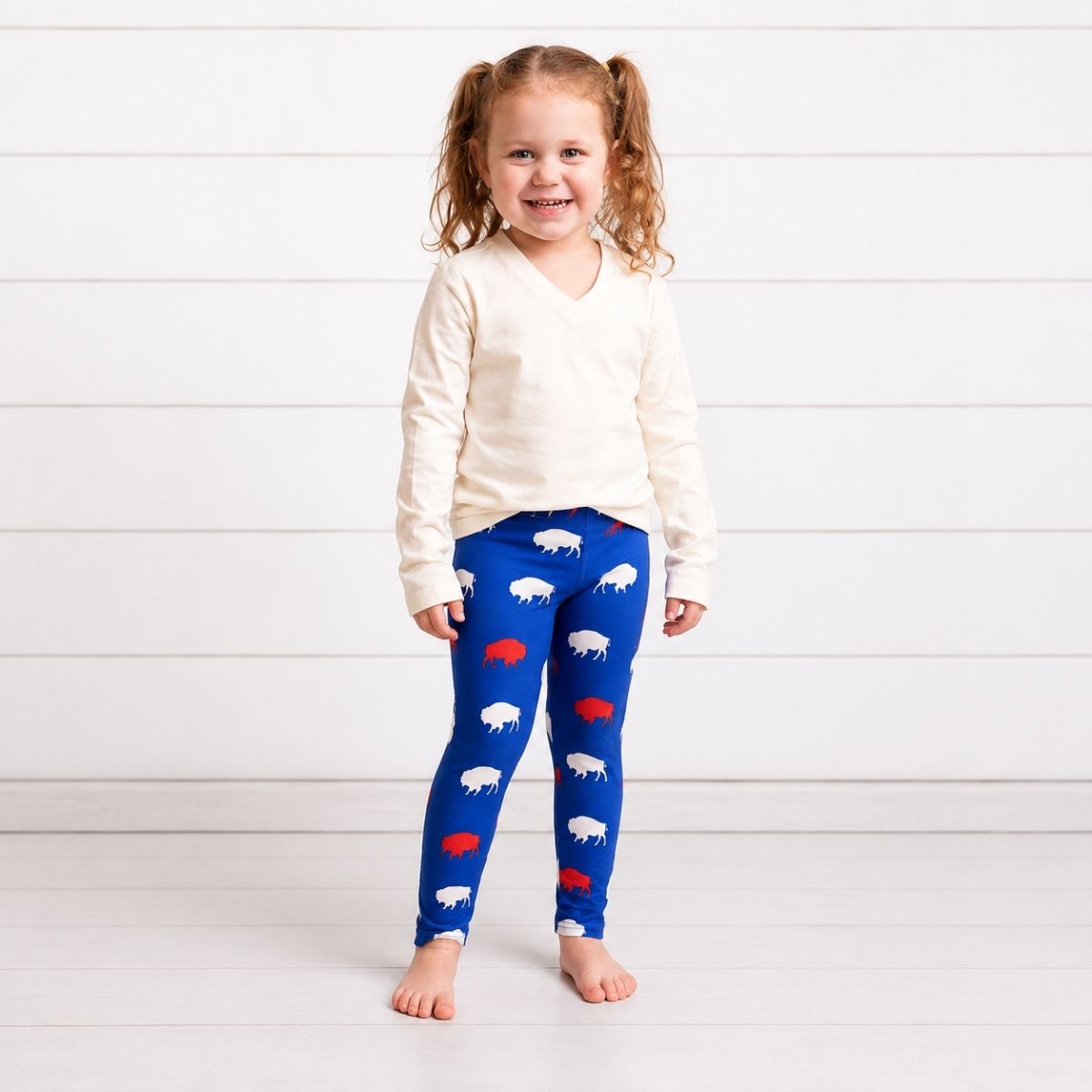 Child wearing royal blue, white, and red buffalo silhouette print leggings and creme top on a white background.