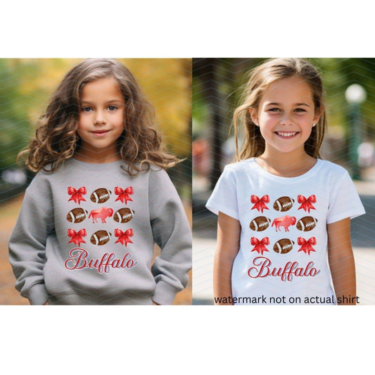 little girls wearing heather gray swatshirt or white tshirt with red bows, buffalo, and brown footballs with the text Buffalo in cursive red and blue below image on fronts. Little Gift Nook