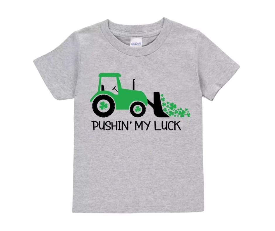 Gray kids tshirt with green tractor, clovers, and pushing my luck on front sitting on white background.