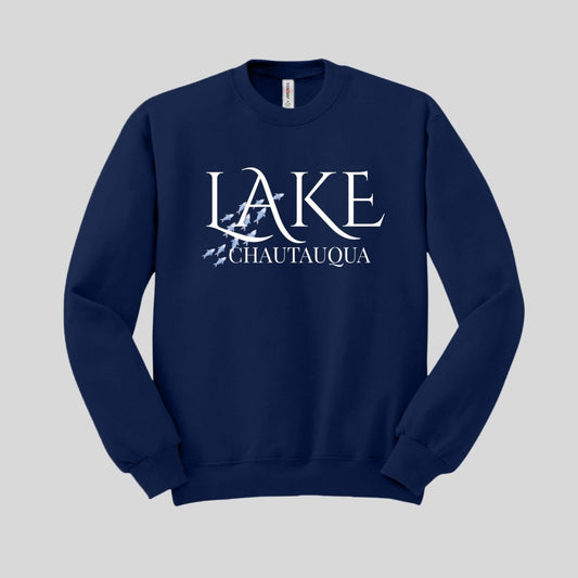 Navy sweatshirt with white text "LAKE CHAUTAUQUA" and blue fish swimming graphic on front laying on gray background. Little Gift Nook