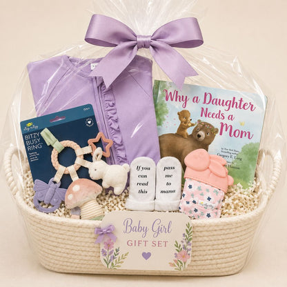 Baby girl gift set with toys, book, and clothing in a basket wrapped with cellophane on a beige background.
