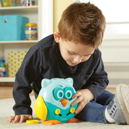 Child playing with Learning Resources Hoot the Owl toy on a carpet in a playroom.