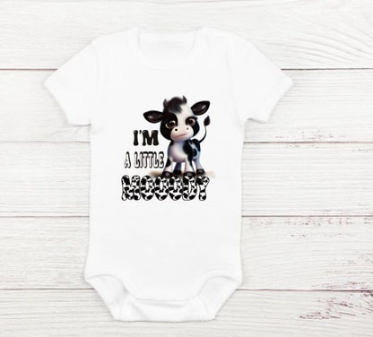 white baby onesie with black white cow and "I'm a little mooody" on front sitting on white wood background.