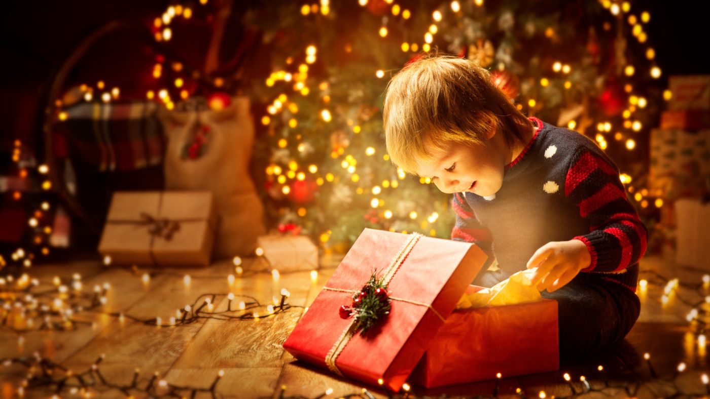 Child opening a gift in a festive setting with Christmas lights and decorations. Little Gift Nook