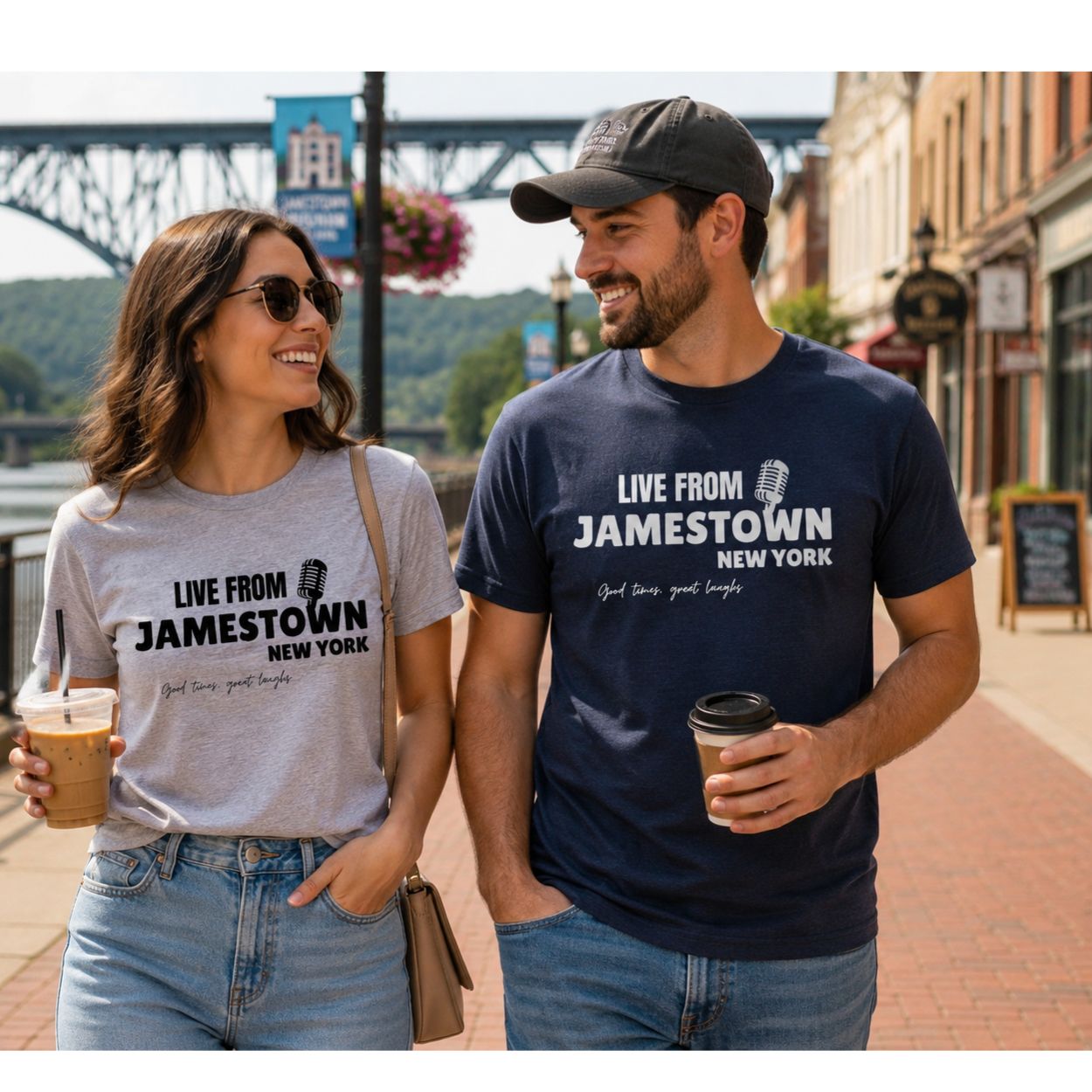Woman and Man wearing "LIVE FROM JAMESTOWN NEW YORK" t-shirts in heather gray and navy walking with coffee on small town street. 