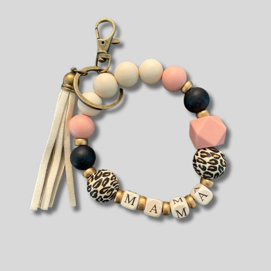 Silicone Beaded Wristlet Mama Keychain. Cream, light pink, black, and animal cheetah print silicone beads with gold painted beads. Cream cubed white beads with MAMA on all sides. Metal keyring and clip, cream tassel. - Little Gift Nook.